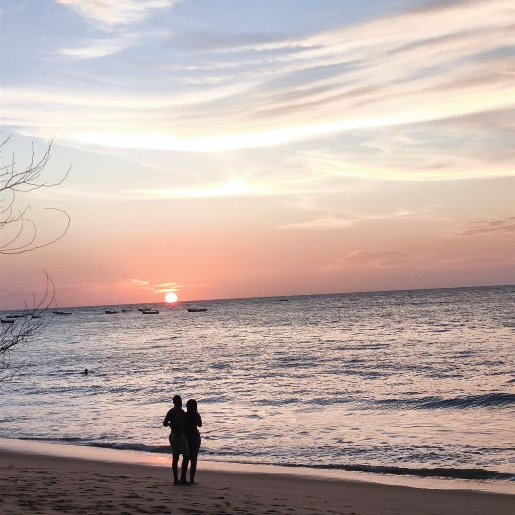 Silhouette eines Paares am Strand bei Sonnenuntergang über dem Meer mit Booten.