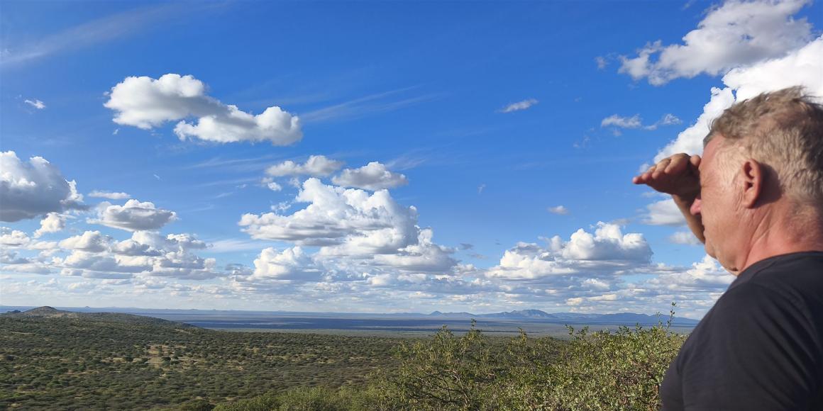 Ein Mann blickt in eine weite, buschige Landschaft unter einem bewölkten Himmel.